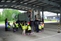 Eine Gruppe Kinder mit gelben Warnwesten umringen neugierig ein Müllfahrzeug